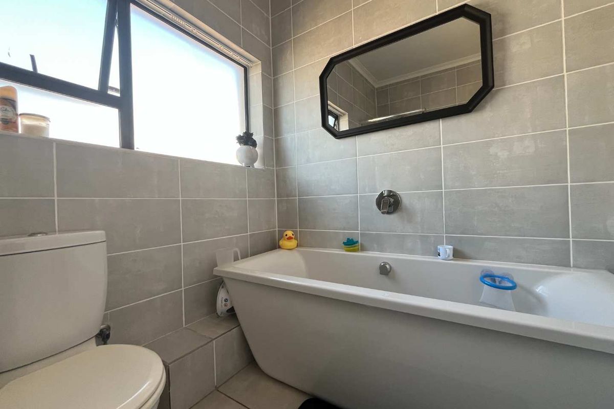 A modern bathroom featuring grey wall tiles, a white bathtub, a wall-mounted faucet, and a toilet.