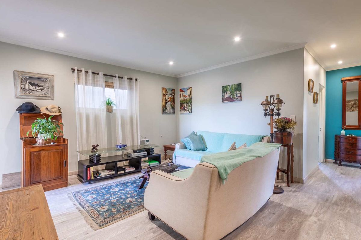 A well-maintained living room featuring light-toned laminate flooring, recessed downlighting, and a neutral color palette with a vibrant blue accent wall.