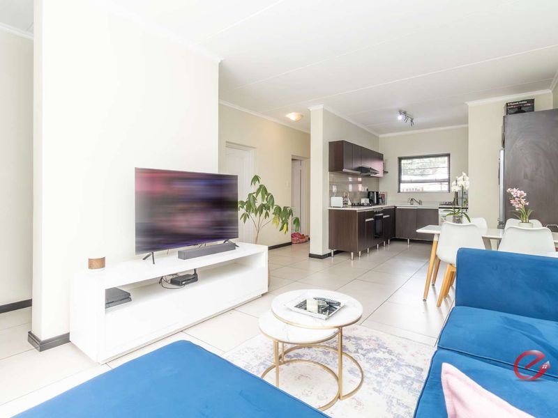 Open-plan living area featuring tiled flooring and a modern kitchen with dark cabinetry, integrated appliances, and a functional layout.