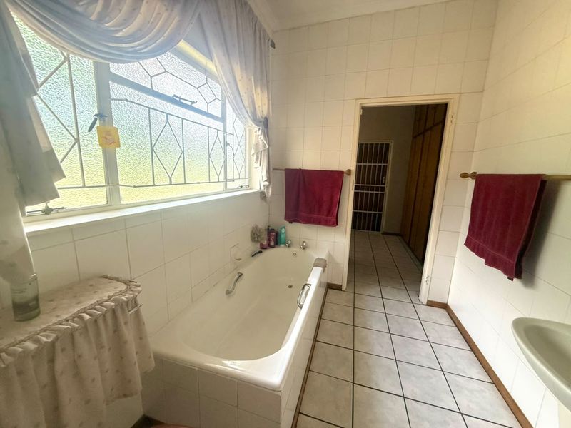 A functional bathroom featuring a built-in bathtub, tiled walls and flooring, and a window with security bars, offering a classic, dated aesthetic.