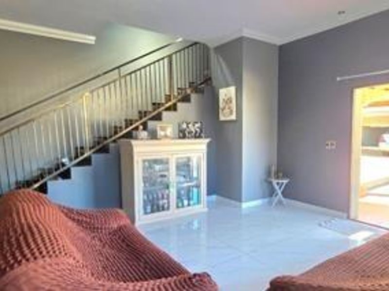 A bright living area featuring tiled flooring, a staircase with a metal balustrade, and direct access to an outdoor space.