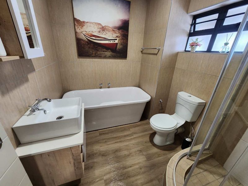 A modern bathroom featuring a freestanding bathtub, vessel sink vanity, corner shower, and neutral wall tiling with wood-look flooring.