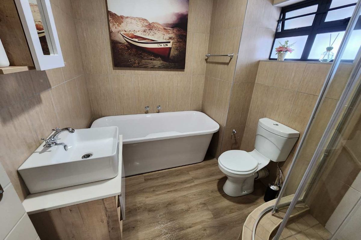 A modern bathroom featuring a freestanding bathtub, vessel sink vanity, corner shower, and neutral wall tiling with wood-look flooring.