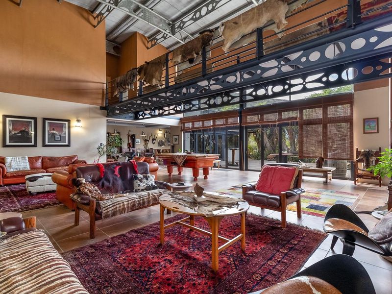 Spacious open-plan living area featuring a mezzanine level, exposed steel structural beams, high vaulted ceilings, and large glass sliding doors leading to the outdoors.