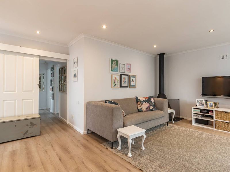A well-maintained living room featuring modern laminate flooring, recessed downlights, a wood-burning fireplace, and a sliding barn door leading to the hallway.