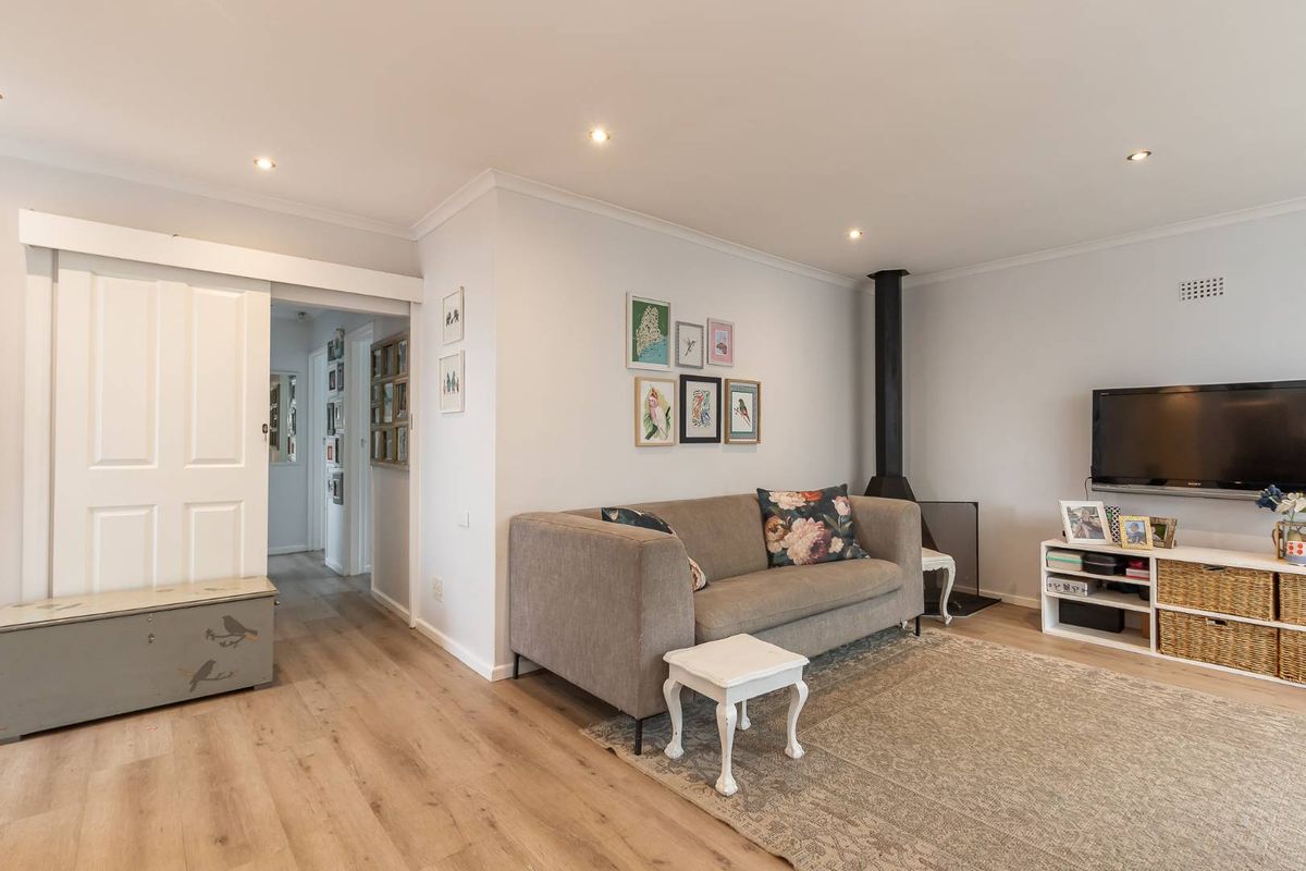 A well-maintained living room featuring modern laminate flooring, recessed downlights, a wood-burning fireplace, and a sliding barn door leading to the hallway.