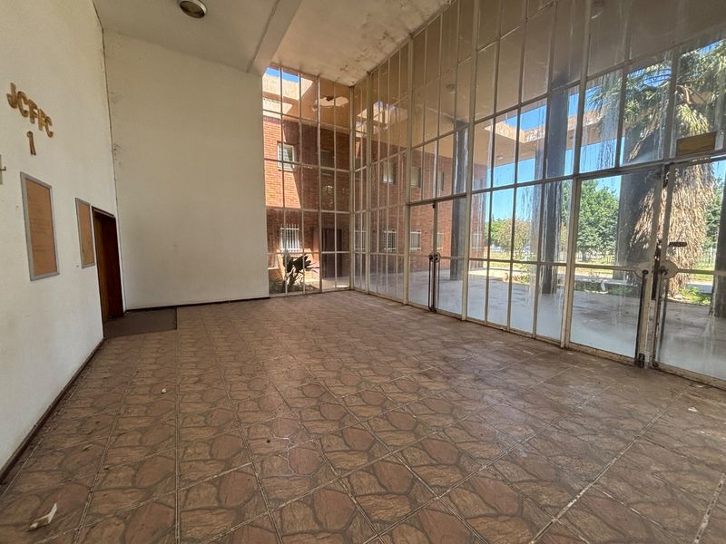 Spacious entrance lobby featuring full-height glass walls, tiled flooring, and direct access to the exterior courtyard, offering significant potential for modernization.
