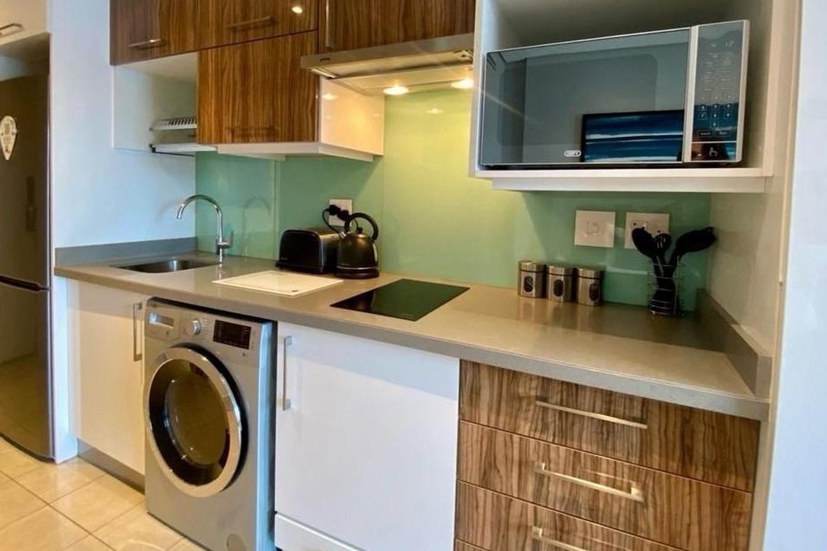 Modern kitchen featuring wood-grain and white cabinetry, stone countertops, glass splashback, integrated hob, extractor fan, and built-in microwave.