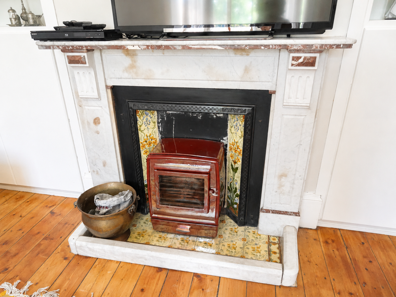 A classic living room feature fireplace with a marble mantel, decorative floral tile surround, and a fitted wood-burning stove set on timber flooring.