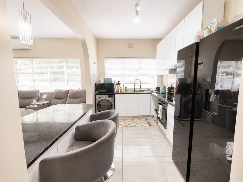 Modern open-plan kitchen featuring sleek white cabinetry, granite countertops, integrated appliances, and tiled flooring, seamlessly flowing into the adjacent living area.