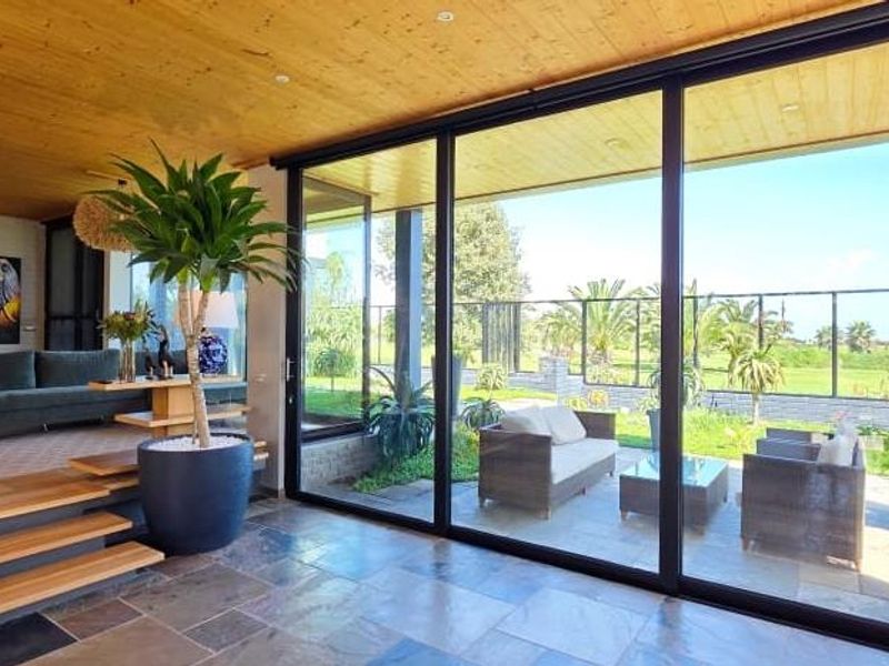 Modern living area featuring natural stone flooring, a warm timber ceiling, and expansive sliding glass doors that provide seamless access to the outdoor patio.