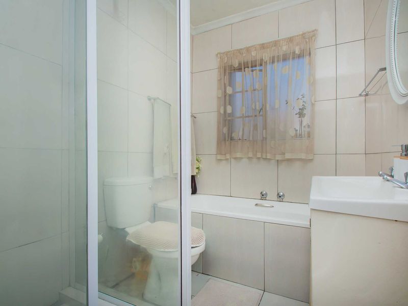 A functional bathroom featuring a shower enclosure, bathtub, toilet, and a vanity basin with tiled finishes throughout.