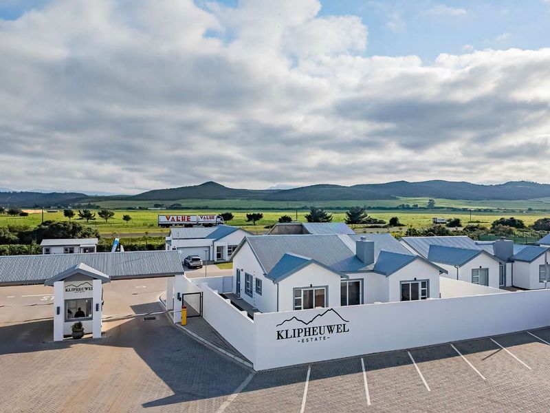 Aerial view of Klipheuwel Estate entrance, featuring a modern security gatehouse, paved parking area, and well-maintained residential units with metal roofing.