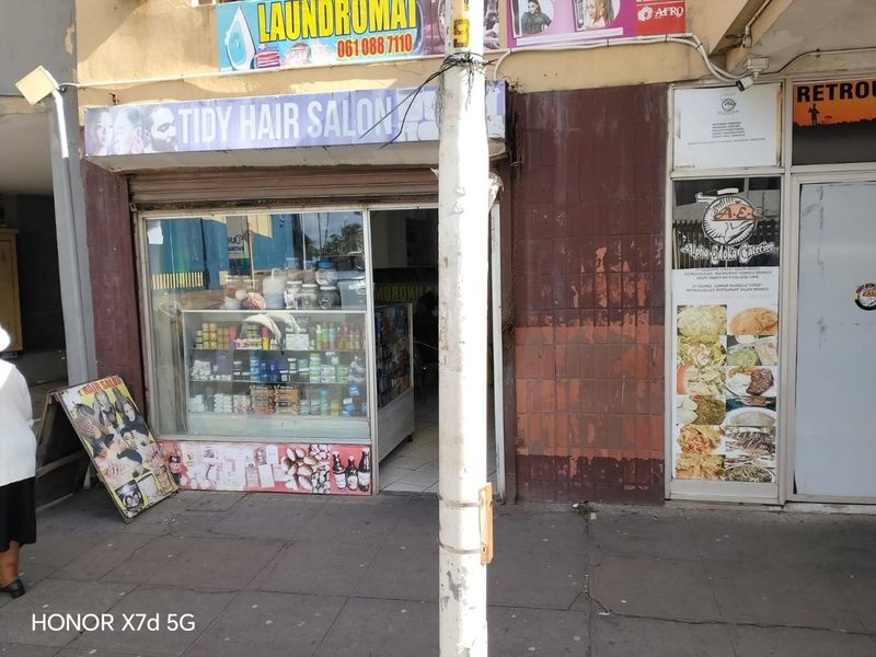 Street-level retail storefront featuring a large display window, metal security shutter, and signage for a hair salon and catering business.