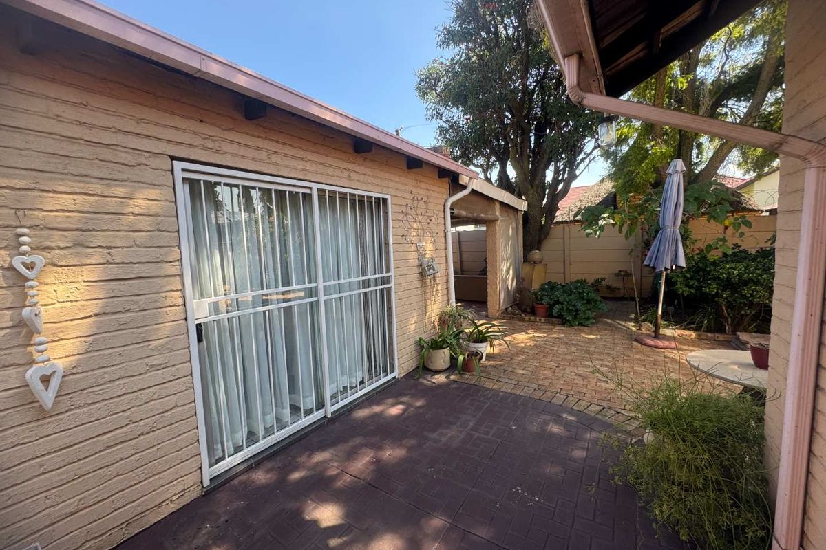 A private rear patio area featuring brick paving, sliding glass doors with security gates, and established garden surroundings.
