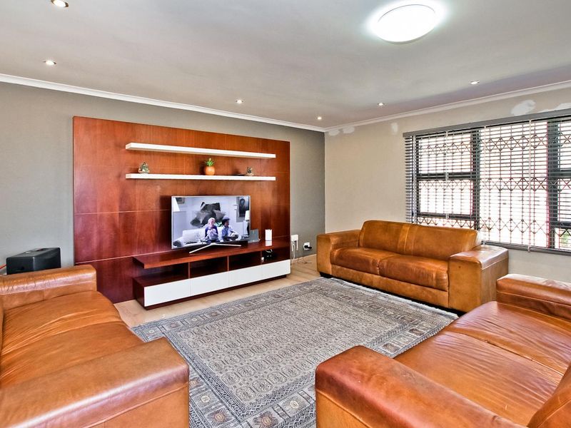 Spacious living room featuring a custom built-in wooden media wall unit, recessed lighting, and large windows with security gates.