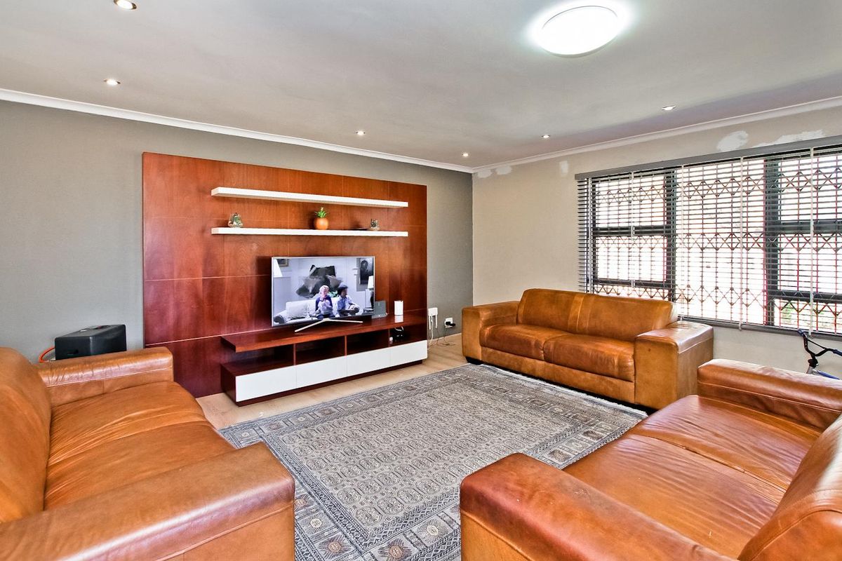 Spacious living room featuring a custom built-in wooden media wall unit, recessed lighting, and large windows with security gates.