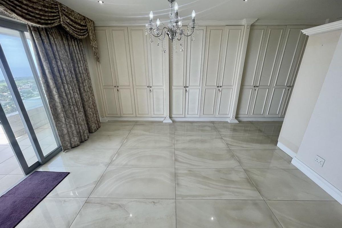 A spacious bedroom featuring large-format polished floor tiles, extensive built-in cabinetry, a decorative chandelier, and sliding glass doors leading to an outdoor balcony.