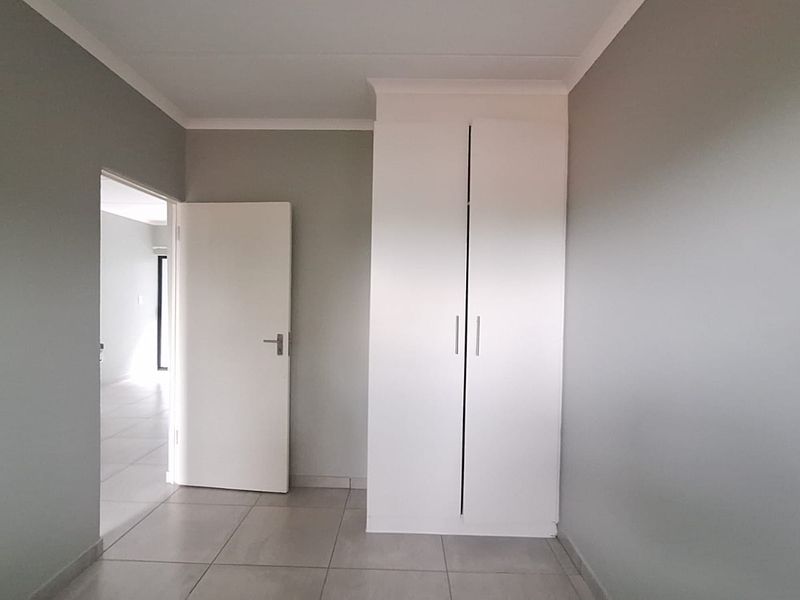 A clean, empty bedroom featuring neutral grey walls, tiled flooring, and a built-in white wardrobe with modern finishes.