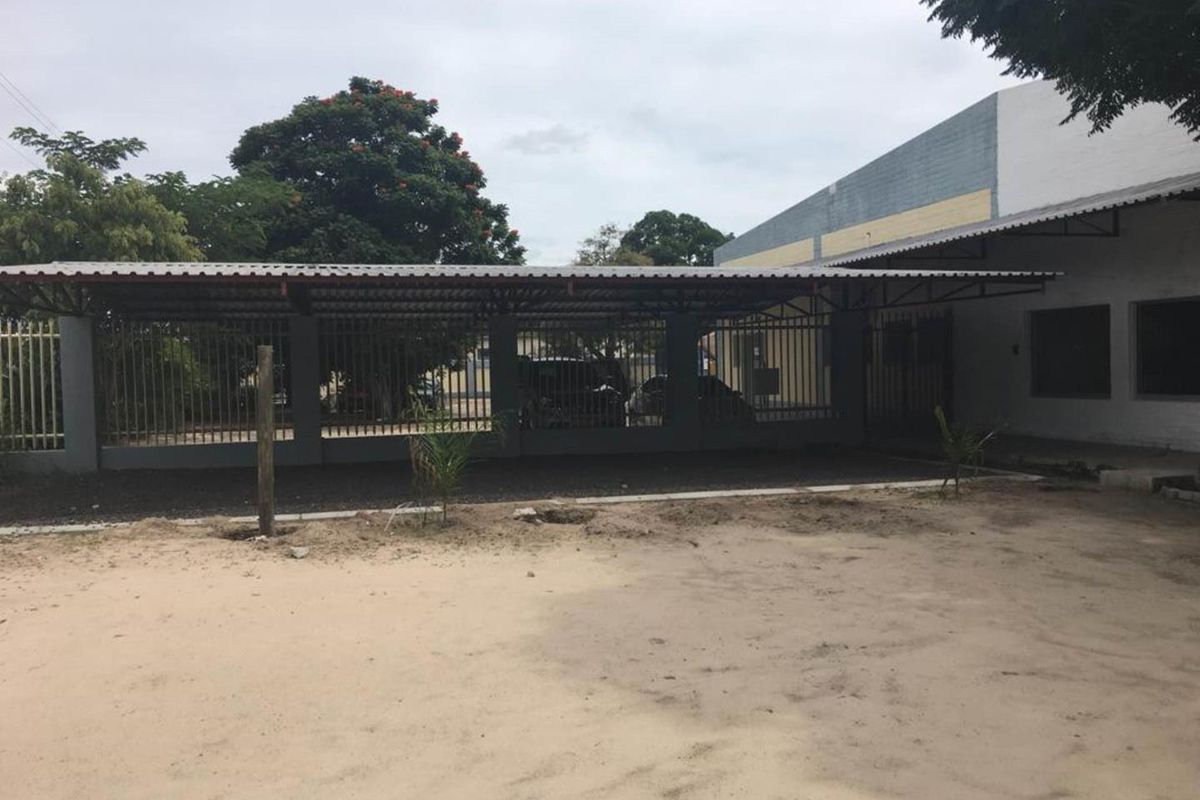 Industrial property exterior featuring a covered parking structure with metal roofing and secure perimeter fencing, set against a large open yard area.