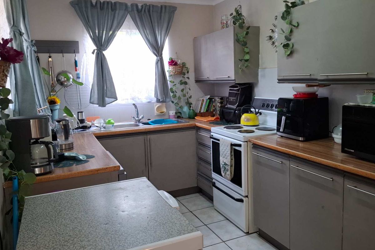 A functional kitchen featuring laminate countertops, built-in cabinetry, a stainless steel sink, and a freestanding stove with tiled flooring.