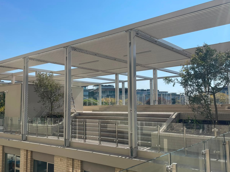 A modern, expansive rooftop terrace featuring a louvred pergola, glass balustrades, and tiered seating areas with integrated planters.