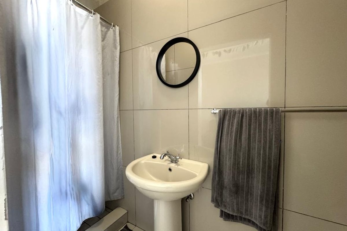 A functional bathroom featuring a pedestal basin, chrome faucet, and full-height wall tiling, with a shower area enclosed by a curtain.