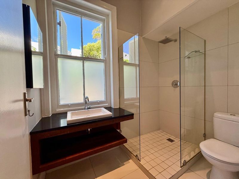 Modern bathroom featuring a walk-in shower with glass screen, a sleek vanity with black stone countertop, and a classic sash window.