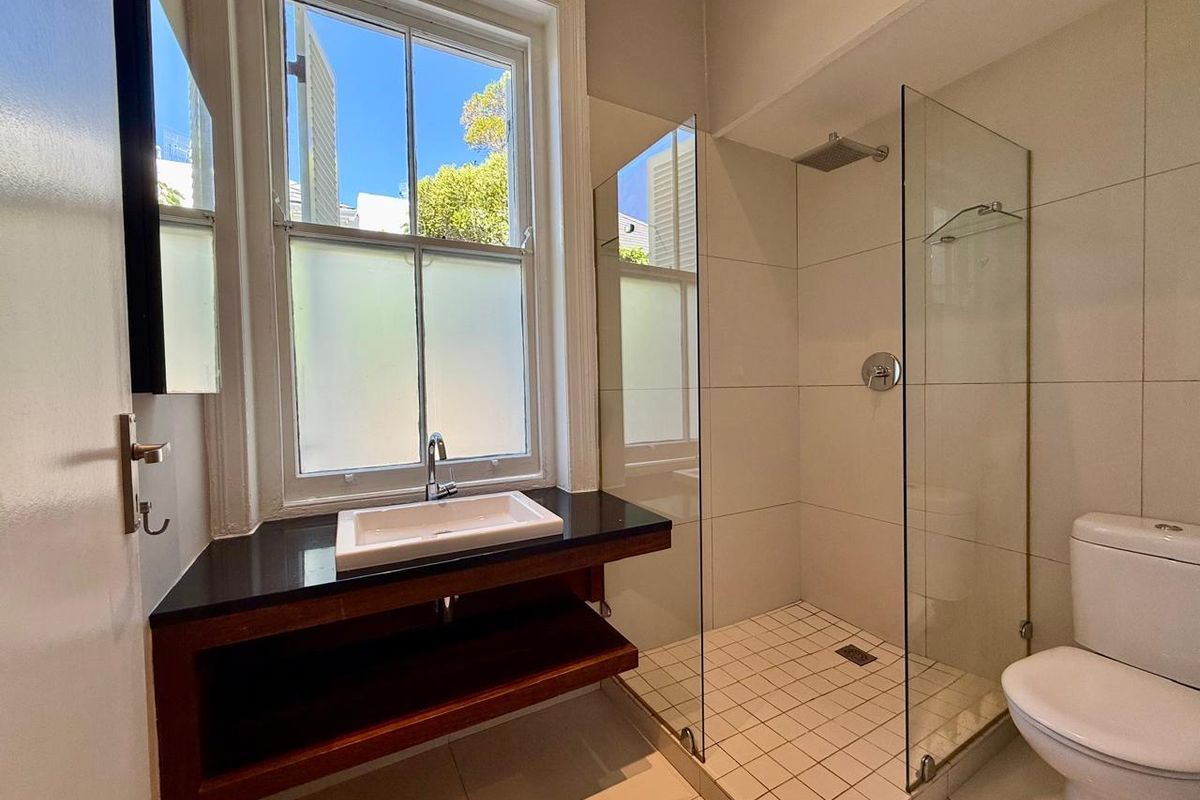 Modern bathroom featuring a walk-in shower with glass screen, a sleek vanity with black stone countertop, and a classic sash window.