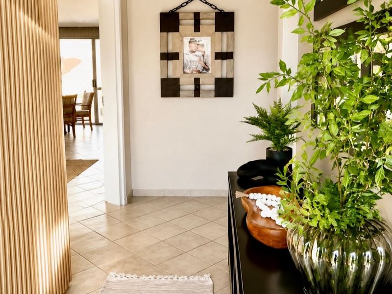 A bright and welcoming entrance hall featuring neutral tiled flooring and a decorative slatted timber room divider leading into the main living area.