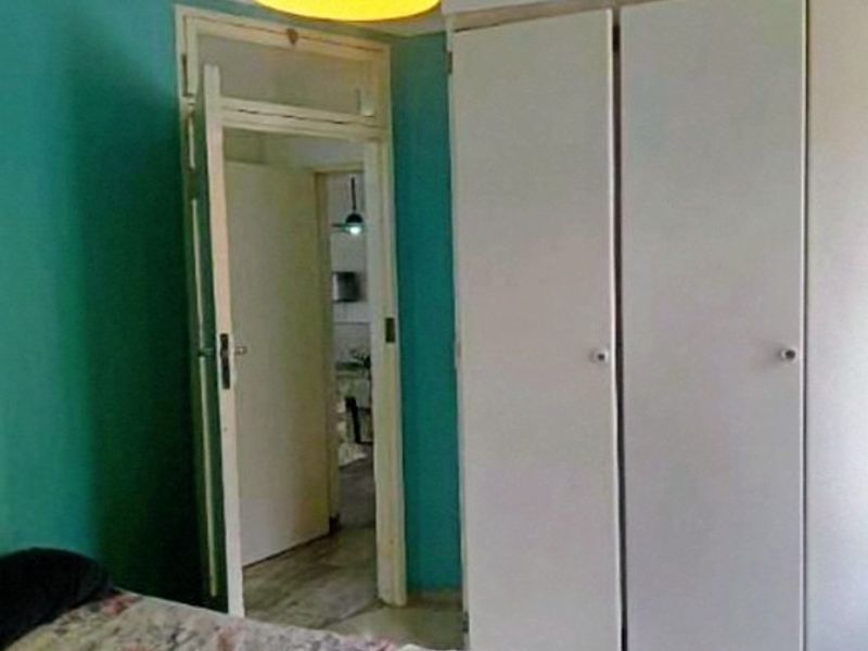 Bedroom featuring built-in cupboards and a doorway leading to an adjacent room, with dated finishes and paintwork.
