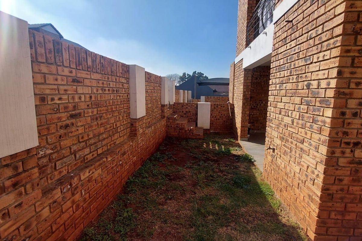 A private rear garden area featuring face-brick boundary walls and a paved section adjacent to the apartment building structure.