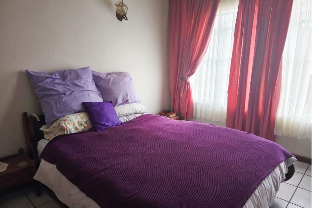 A bedroom featuring tiled flooring and a wall-mounted light fixture, offering a functional space with natural light from the window.