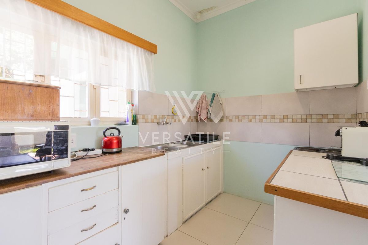 A compact kitchen featuring white cabinetry, tiled splashbacks, and a functional layout with a window overlooking the exterior.