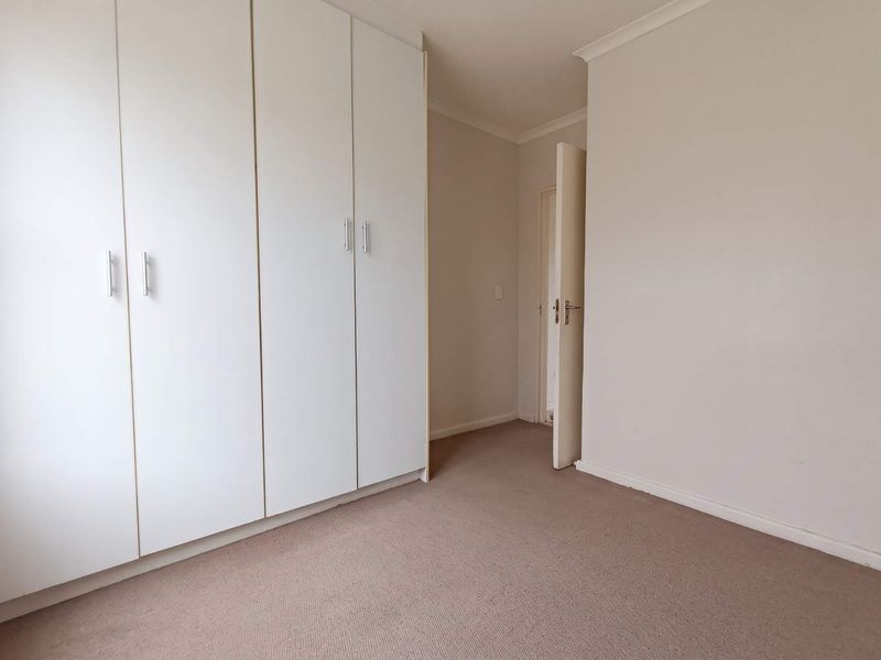 A clean, empty bedroom featuring neutral walls, carpeted flooring, and ample built-in cupboard storage space.