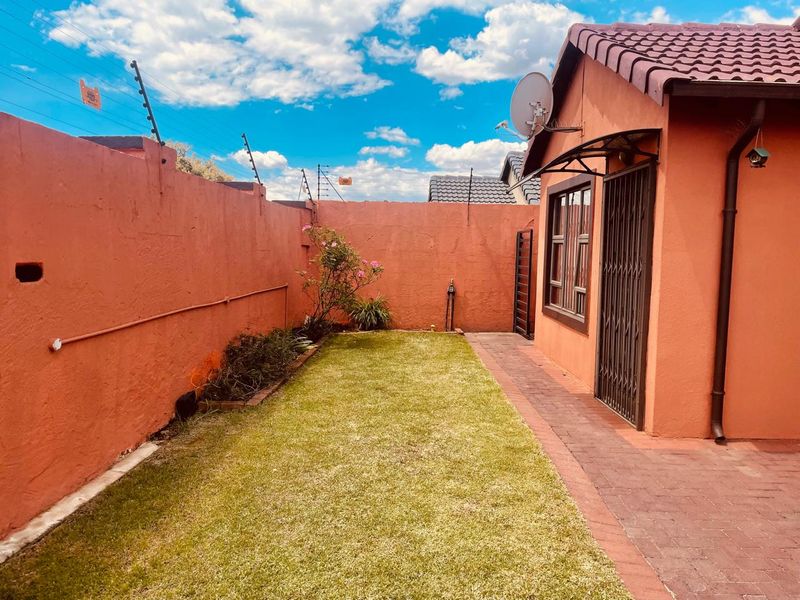 A private rear garden featuring a paved walkway, lawn area, and high boundary walls secured with electric fencing.