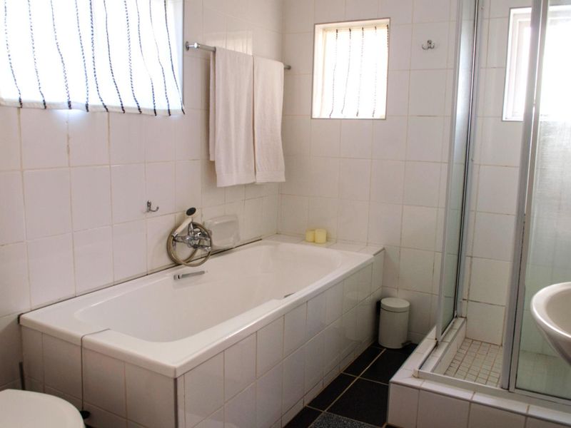 A functional bathroom featuring a built-in bathtub, separate shower enclosure, and white wall tiling with contrasting dark floor tiles.