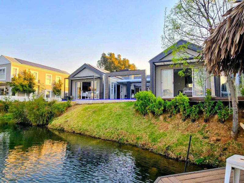 A scenic view of the rear exterior featuring a waterfront deck, a thatched gazebo, and modern residential structures with sliding glass doors.