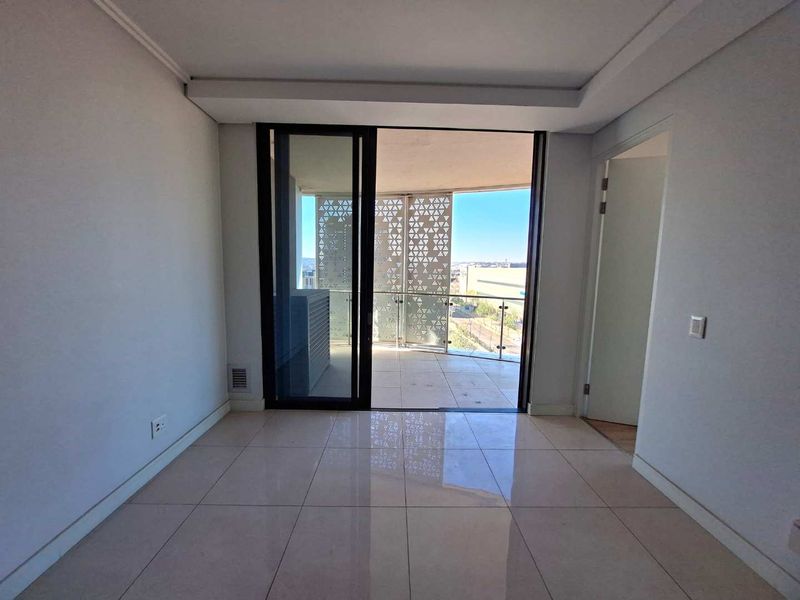 Bright, empty living area featuring large sliding glass doors that open onto a private balcony with decorative metal screening and city views.