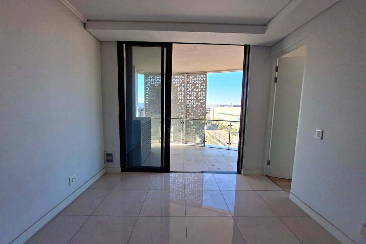 Bright, empty living area featuring large sliding glass doors that open onto a private balcony with decorative metal screening and city views.