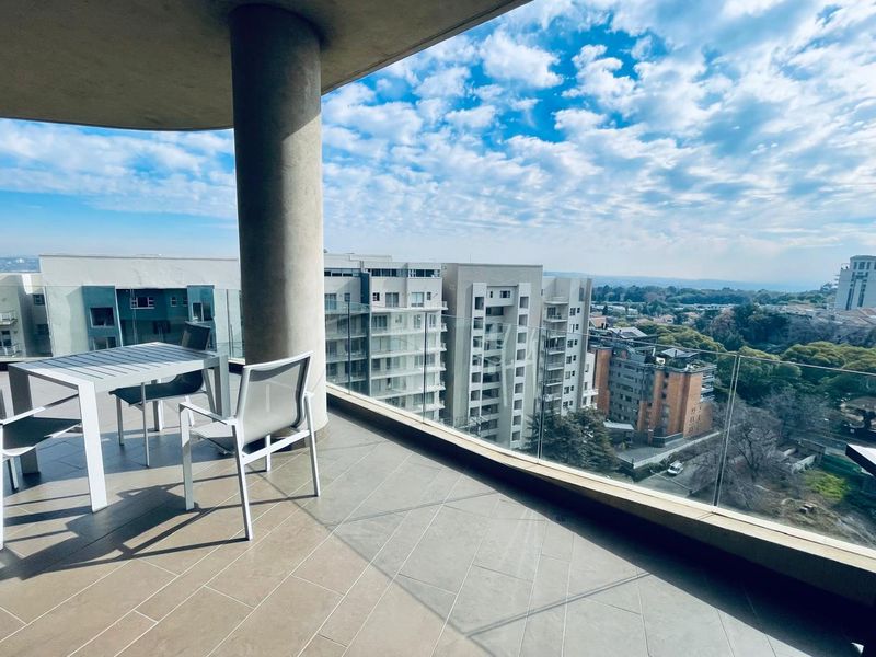 A spacious balcony featuring modern tiled flooring, a structural concrete column, and a sleek glass balustrade offering expansive urban views.