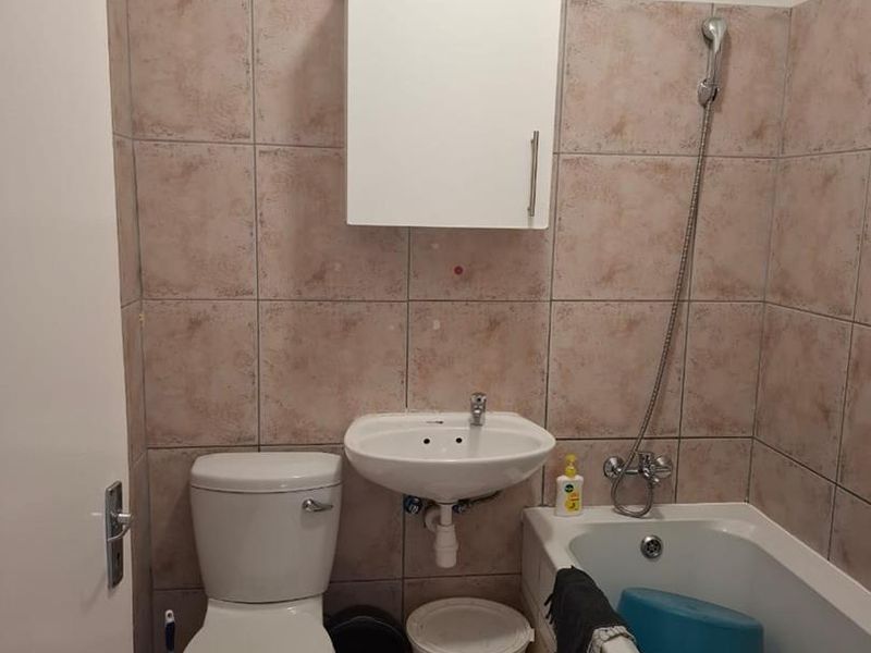 Compact bathroom featuring a bathtub with shower mixer, wall-mounted basin, toilet, and tiled finishes. Requires cosmetic updates to improve aesthetic appeal.