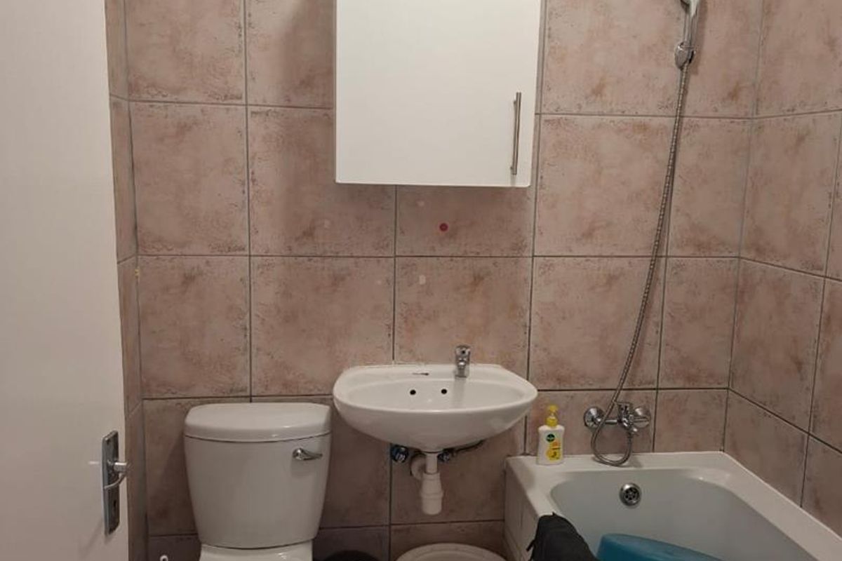 Compact bathroom featuring a bathtub with shower mixer, wall-mounted basin, toilet, and tiled finishes. Requires cosmetic updates to improve aesthetic appeal.