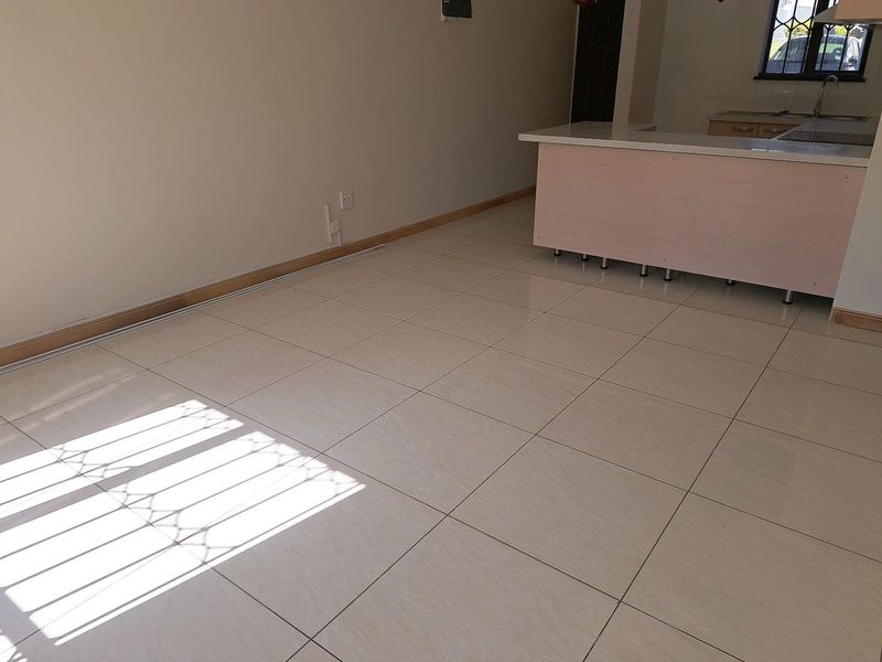 An open-plan living and kitchen area featuring neutral tiled flooring, a kitchen island, and security bars on the windows.