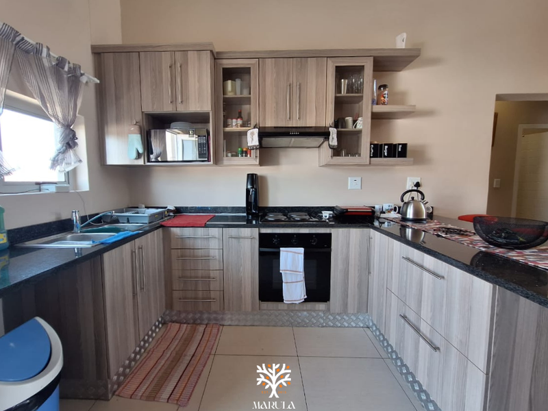 A functional kitchen featuring wood-grain cabinetry, granite countertops, integrated oven, extractor fan, and built-in microwave with tiled flooring.