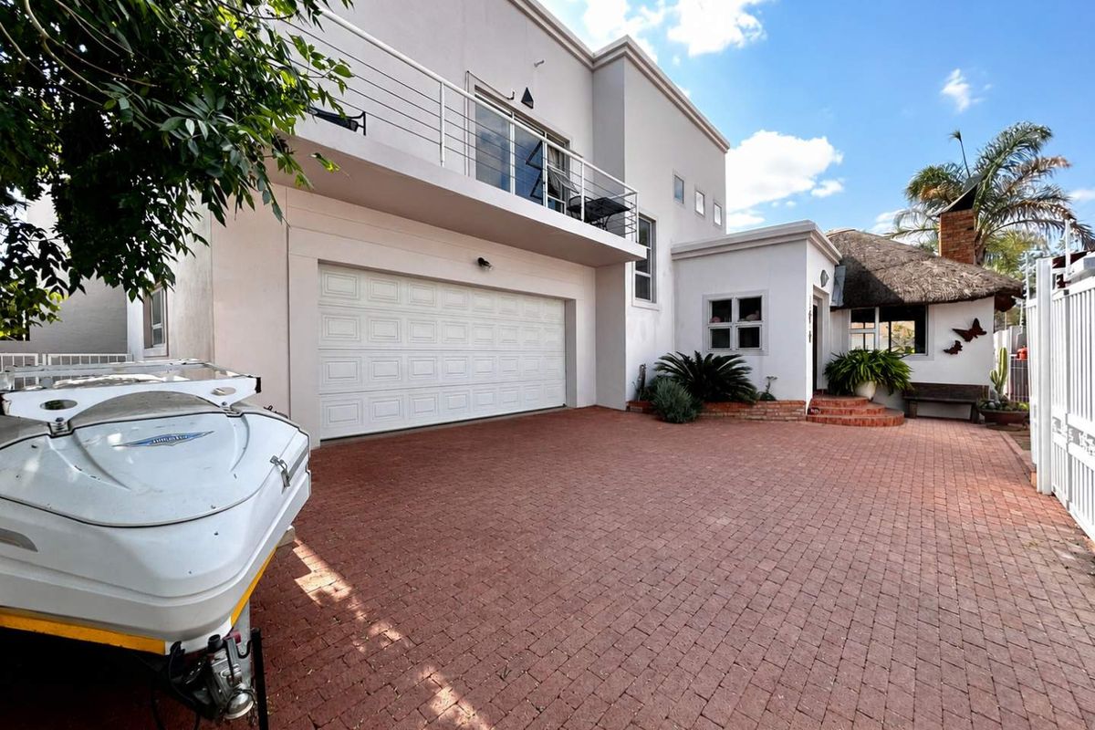 Front exterior view of the property featuring a paved driveway, double garage, and an upper-level balcony with metal railings.