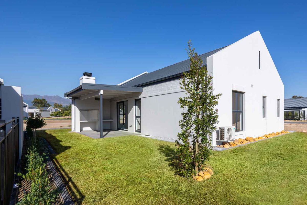 A modern rear exterior view of the house featuring a covered patio with a built-in braai, neat lawn, and clean white facade.
