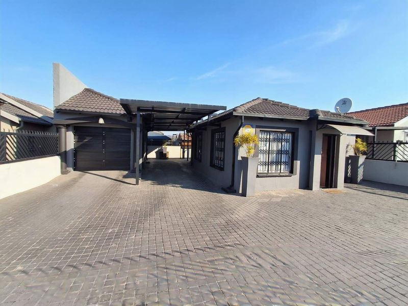 Front exterior view of the house featuring a paved driveway, covered carport, single garage, and secure window gates.