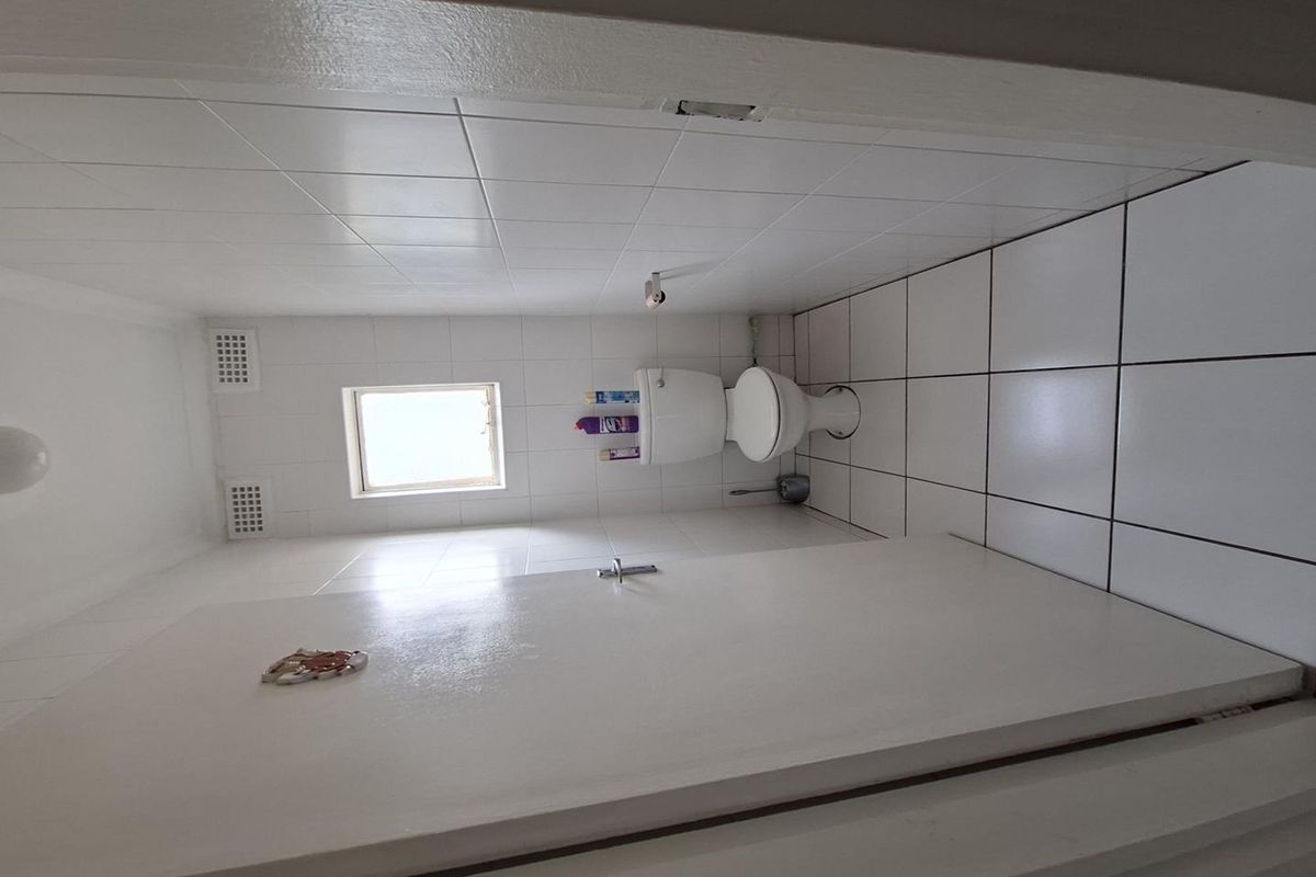 A functional bathroom featuring white ceramic wall and floor tiles, a standard toilet, and ventilation grilles.