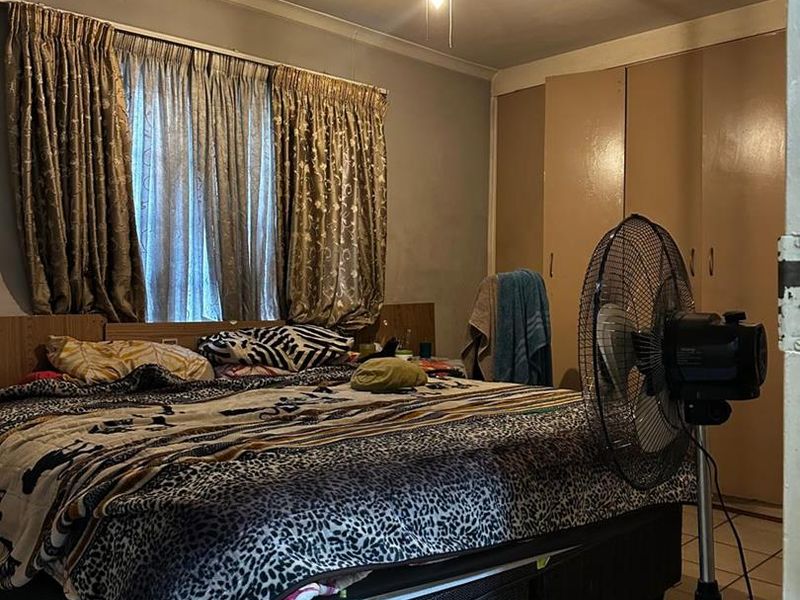 A bedroom featuring tiled flooring, a ceiling fan, and built-in cupboards, offering a functional space with standard finishes.